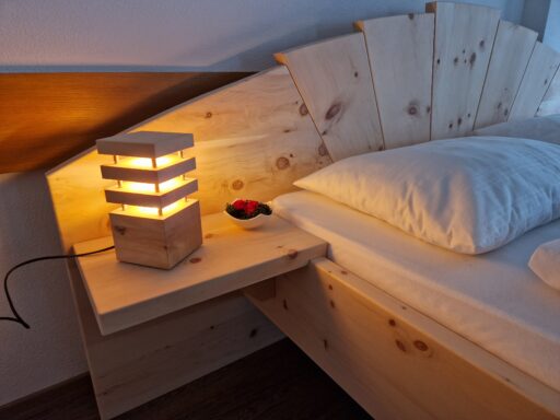 Zirbenlampe auf einem Nachtkästchen neben einem Zirbenbett