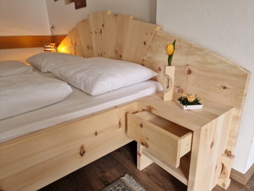 Zirbenbett mit Nachtkästchen und geöffneter Schublade