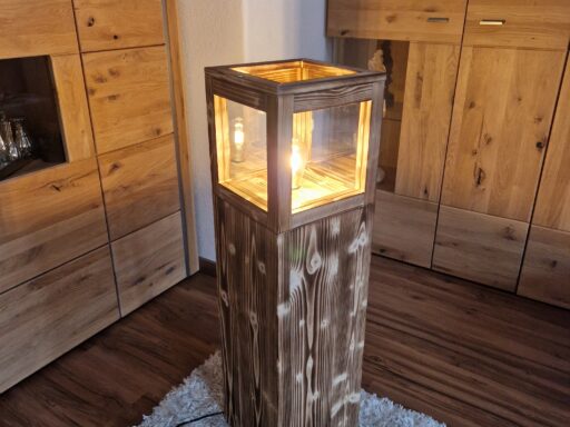 Stehlampe Flame aus Zirbenholz, beleuchtet im Wohnraum