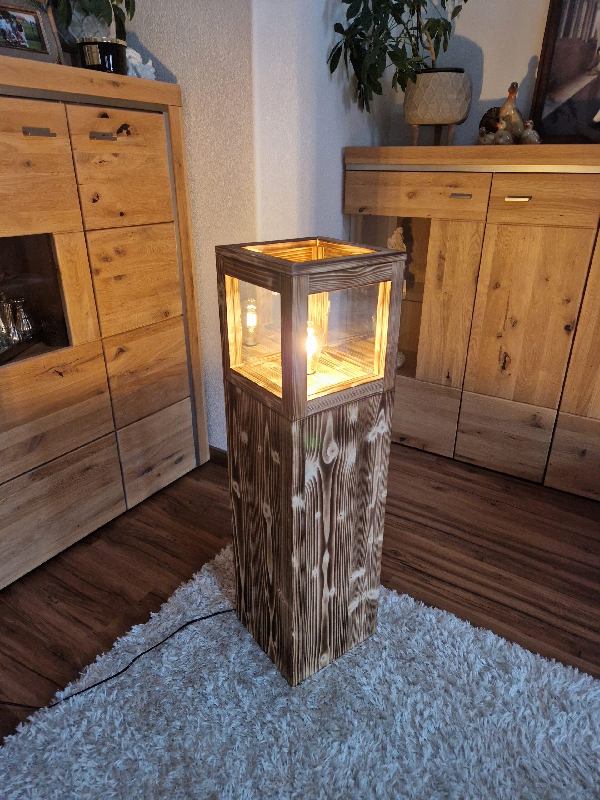 Stehlampe Flame aus Zirbenholz, beleuchtet im Wohnraum