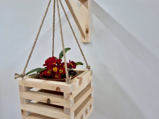 Blumenampel aus Zirbenholz an der Wandhalterung, bepflanzt mit roter Primel