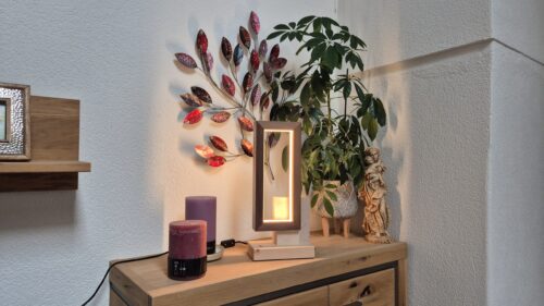Tischlampe aus Zirbenholz, beleuchtet auf einer Kommode neben einem Wandbild