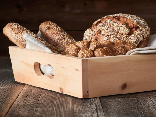Brotkorb aus Zirbenholz mit frischem Brot und Gebäck auf einem Holztisch