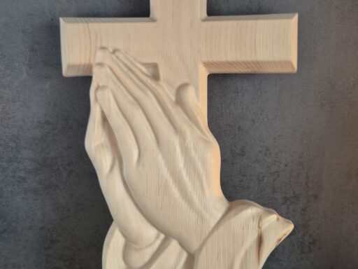 Wandkreuz aus Zirbenholz mit betenden Händen vor dunklem Hintergrund