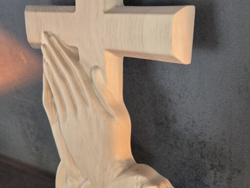 Wandkreuz aus Zirbenholz mit betenden Händen, schräge Ansicht mit Lichtreflex